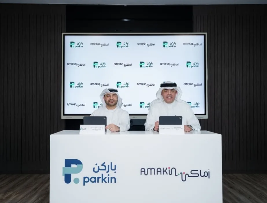 Executives from Parkin and Amakin shake hands in a modern office to celebrate their new regional parking partnership.