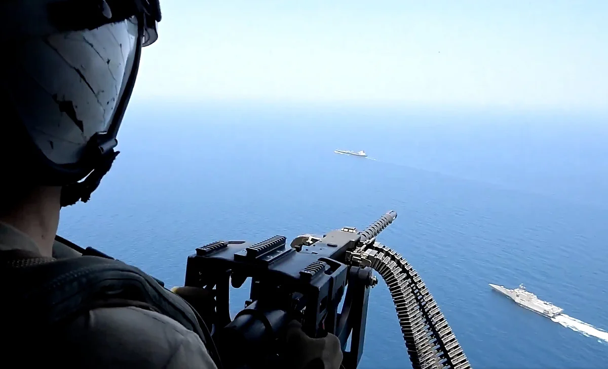 A large oil tanker sails through deep blue waters, leaving a white wake behind its stern under a clear sky.