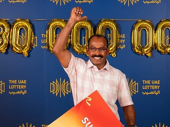 A smiling man in a suit holds a celebratory oversized ceremonial check worth thirty million dirhams.