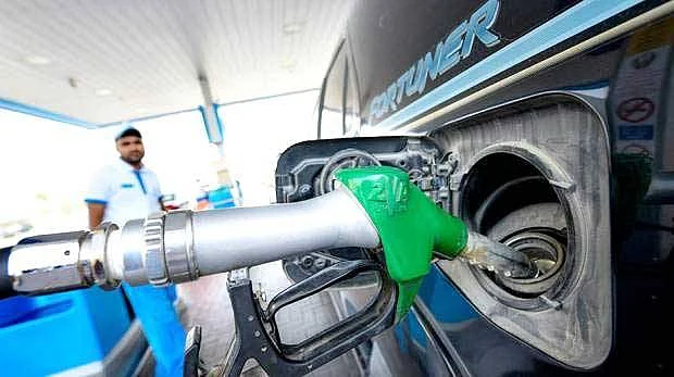 A close-up view of a fuel nozzle being inserted into a car at a gas station under bright daylight.