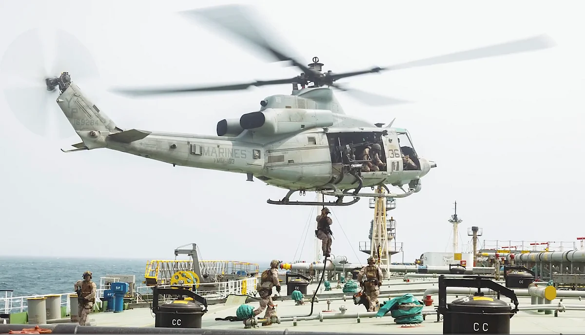 US Marines in tactical gear board a large commercial tanker ship from a speed boat on choppy blue water.