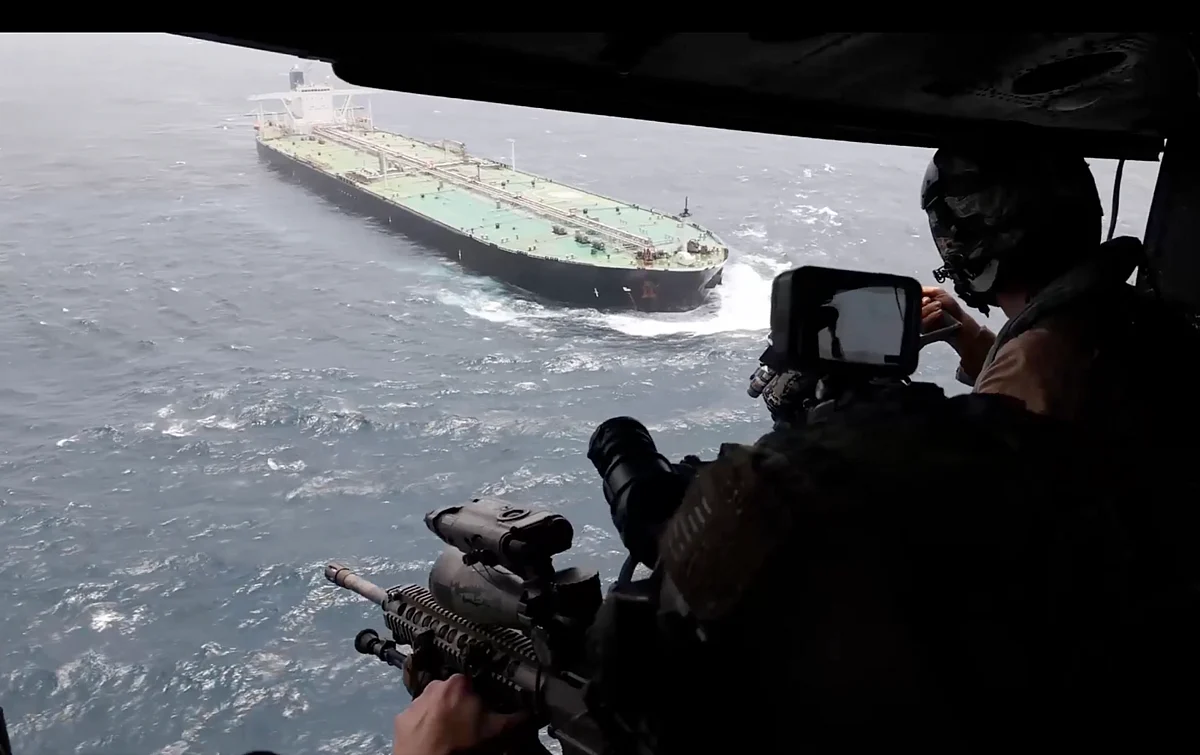 A large grey Navy destroyer sails through choppy deep blue waters under a clear, vast sky.