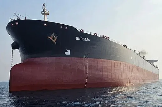Large red and white oil tanker navigates through calm blue ocean waters under a clear and hazy sky.