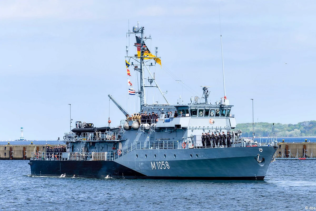 A grey German frigate sails across open blue water under a clear sky during a maritime mission.