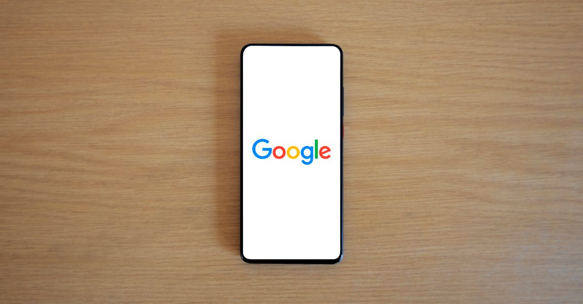 A bright Google logo glows on a sleek smartphone screen held against a blurry city business district background.