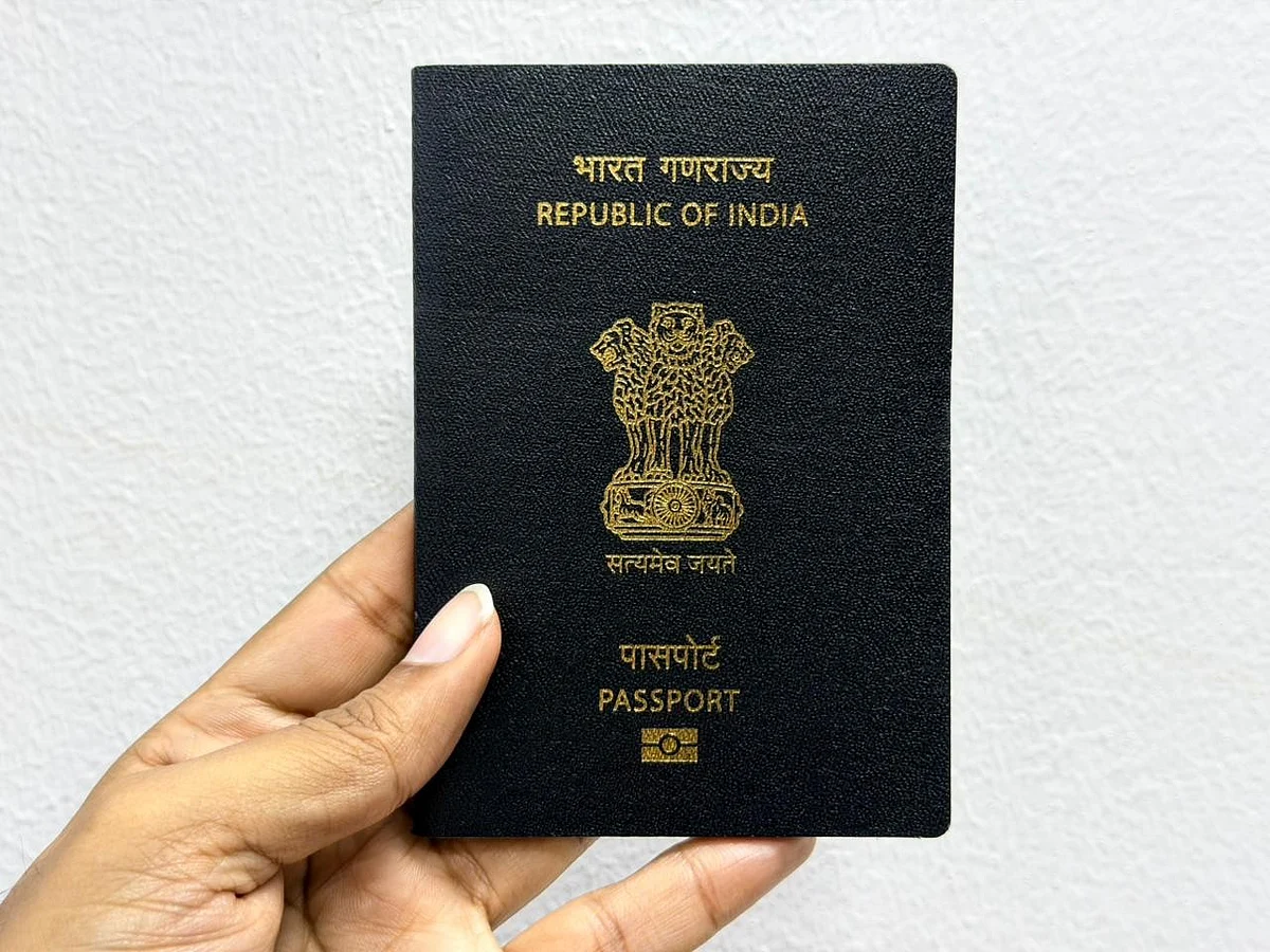 A blue Indian passport sits on a desk beside a pair of glasses and a black fountain pen.