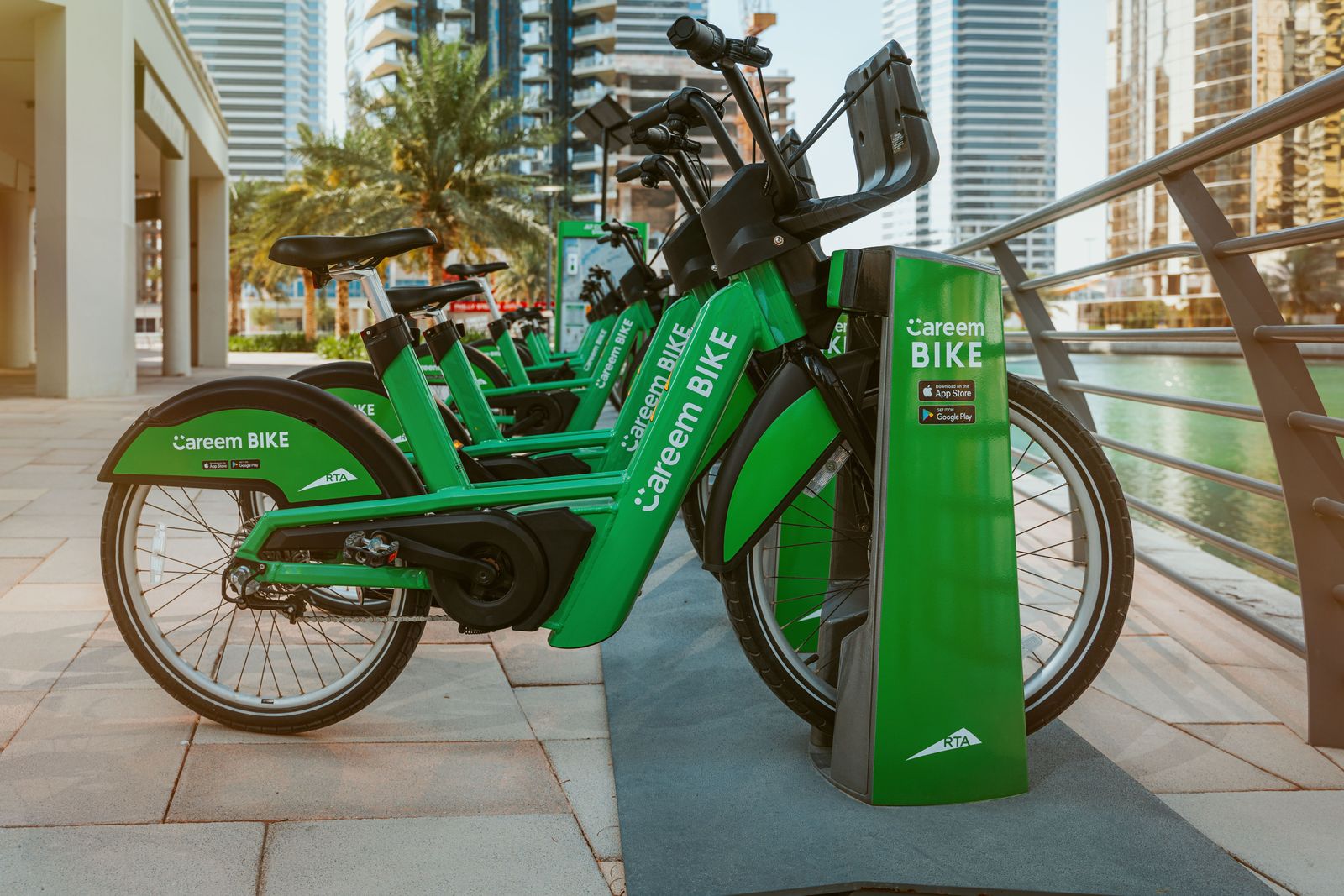 A delivery rider in a safety helmet rides a turquoise Careem e-bike down a sunlit city street in Dubai.