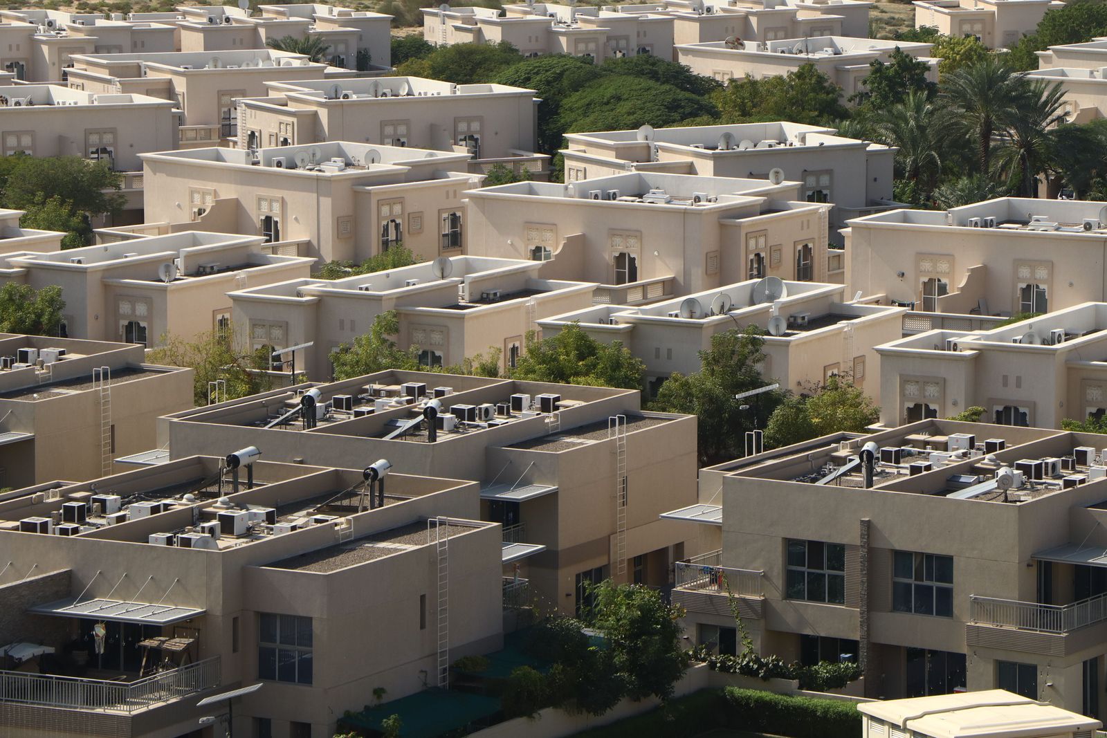 Rows of parked cars line a residential street in Dubai near modern apartment buildings under a clear blue sky.