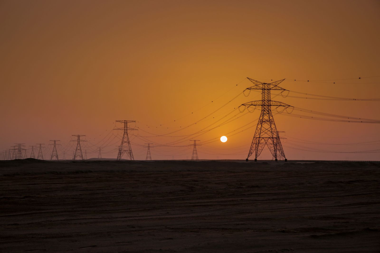 A digital dashboard displays fluctuating global oil prices alongside a row of industrial storage tanks at dusk.