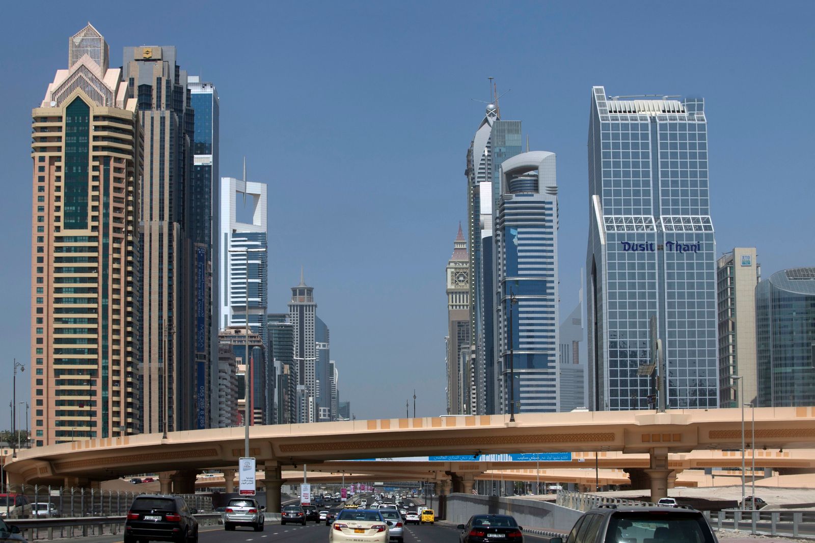 A wide-angle view of the bustling Dubai International Airport terminal with travelers walking near gates and aircraft.