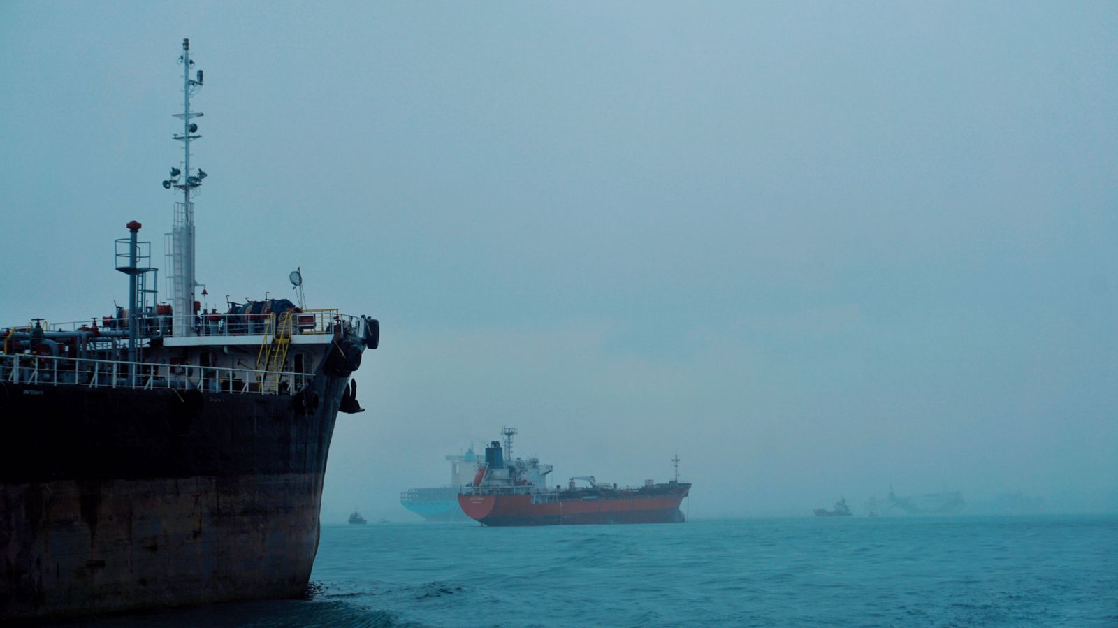 A gray U.S. Navy destroyer cruises through choppy blue waters alongside a large black oil tanker in the open sea.