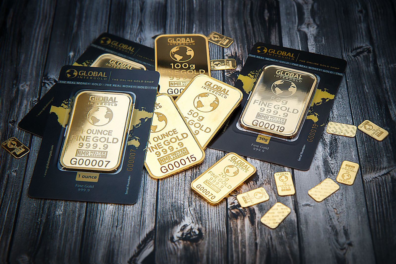 Close-up of shimmering gold bars stacked in rows next to a pile of loose silver coins on a dark surface.