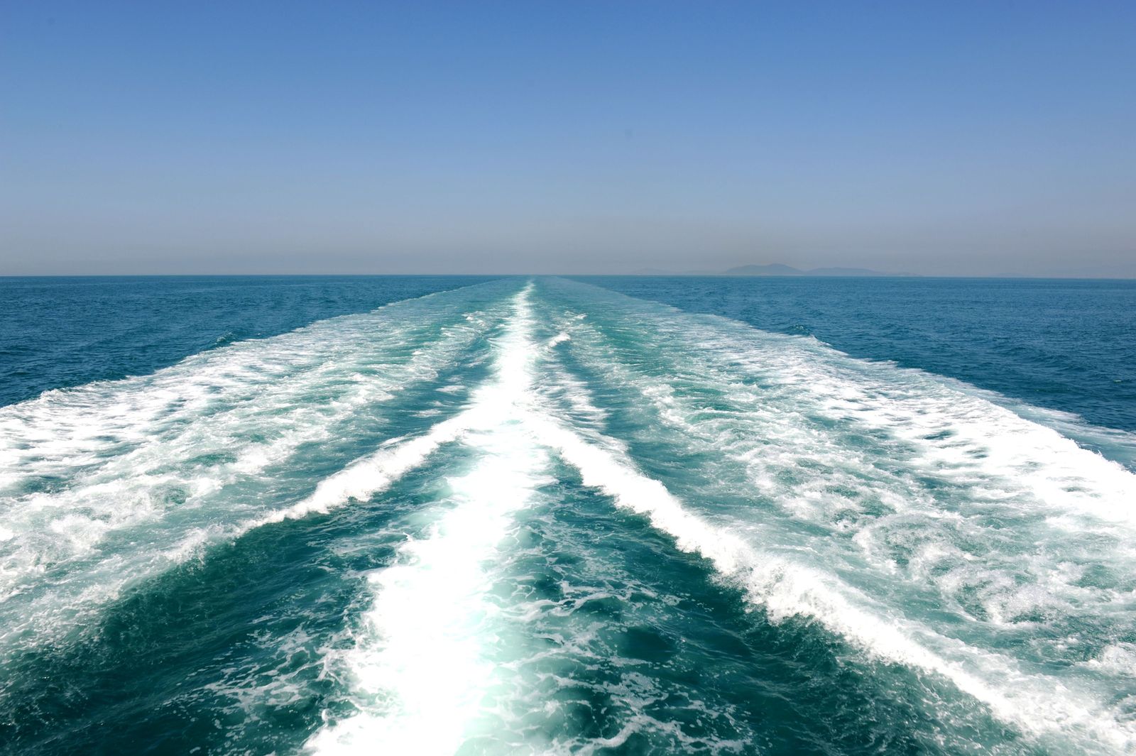 Oil tankers navigate the narrow blue waters of the Strait of Hormuz between rugged, arid mountain coastlines.