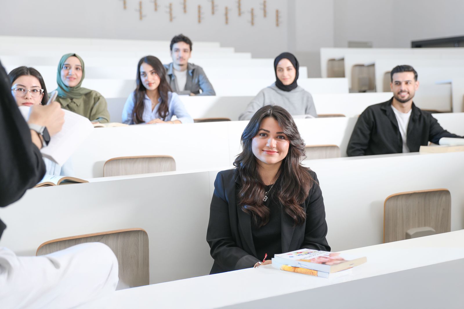 Diverse students walk across the modern Ajman University campus grounds beneath bright blue skies.
