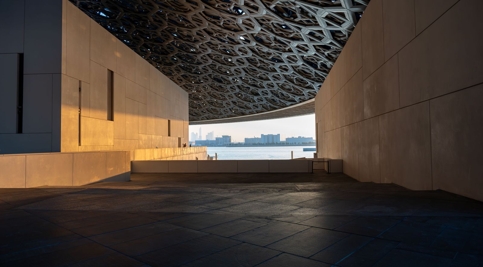 A futuristic architectural model of a modern cityscape sits on a pedestal under bright exhibition hall lights.