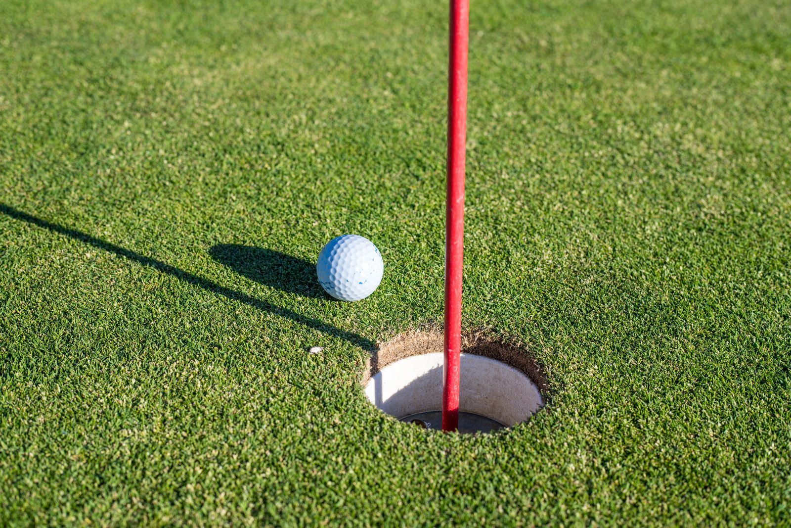 A man swings a golf club on a green course during a professional LIV Golf tournament under a bright sun.