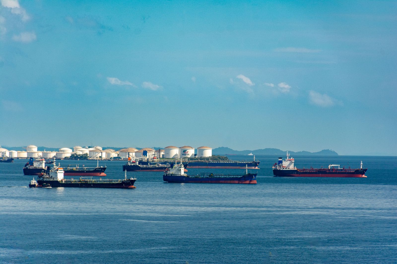 A massive oil tanker billows thick black smoke into the sky while drifting across the calm blue ocean.
