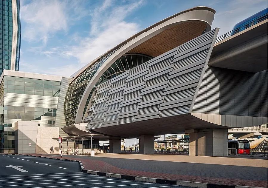 Crowds walk across the glass-walled pedestrian bridge connecting the Burj Khalifa metro station to Downtown Dubai.
