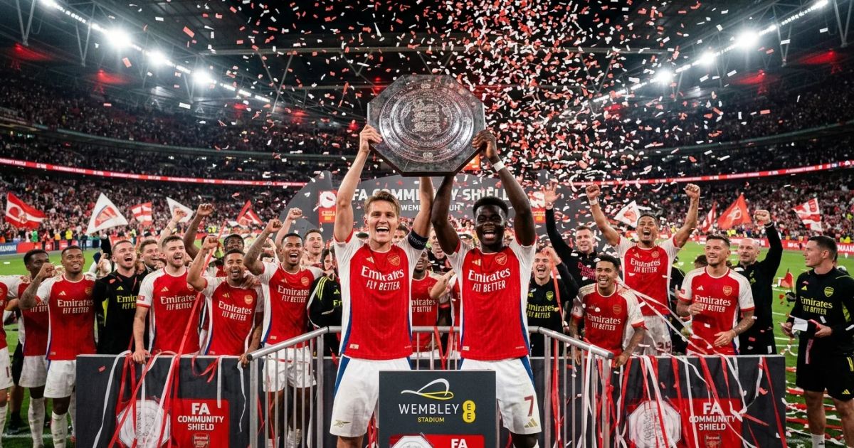 Arsenal players celebrate with the Community Shield trophy on a podium at Wembley Stadium amid red confetti.