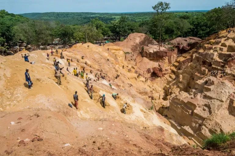 Rescue workers and volunteers dig through a massive crater of red earth at a collapsed artisanal mine site.