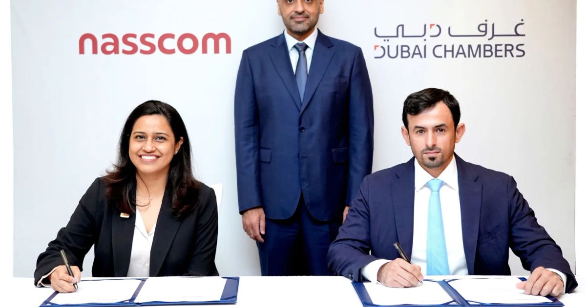 Representatives from Dubai Chambers and NASSCOM shake hands while holding signed documents at a formal business ceremony.