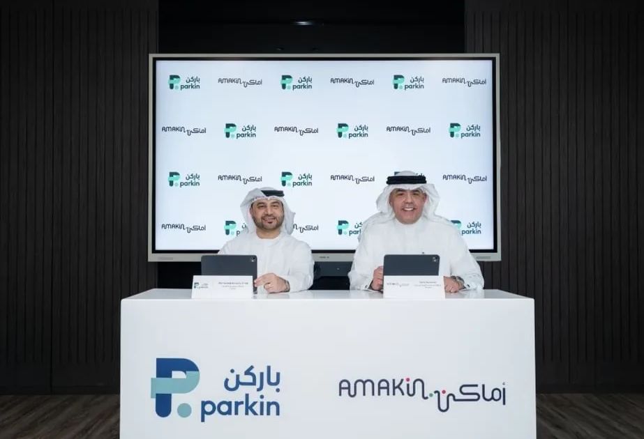 Executives from Parkin and Amakin shake hands in a modern office to celebrate their new regional parking partnership.