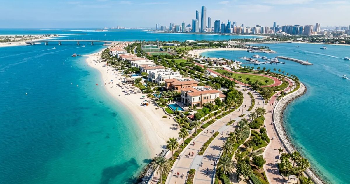 Modern luxury villas and manicured green spaces overlook a calm turquoise waterfront under a clear blue sky.